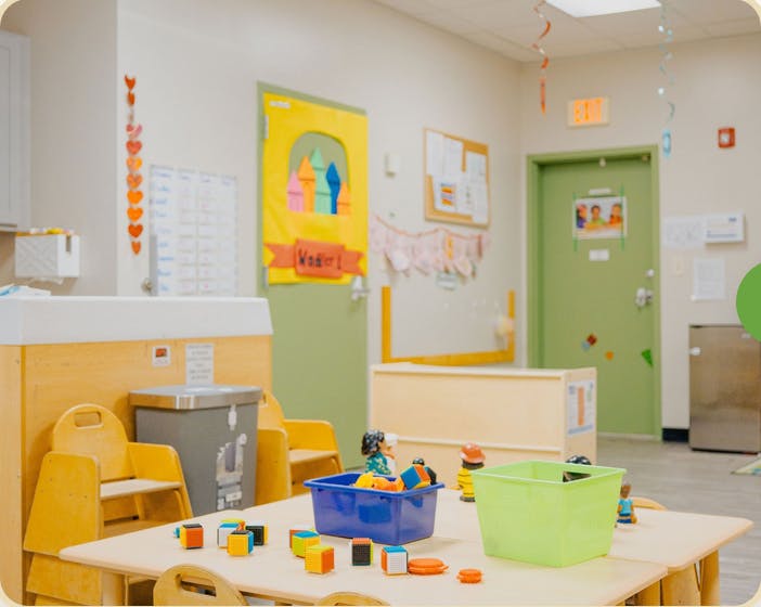 Classroom with small tables and chairs, toys on a table, and decorated doors