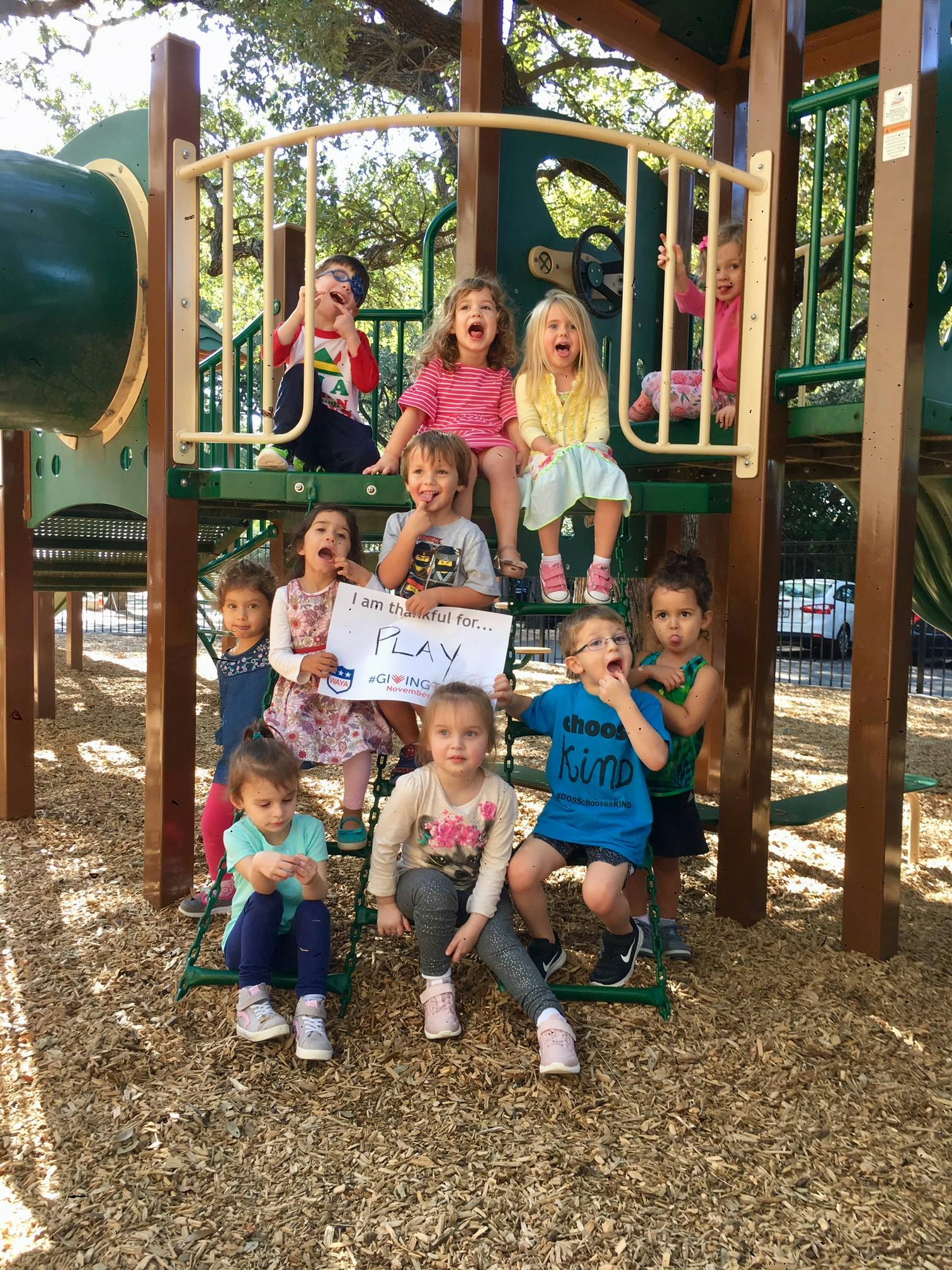 Children on and around a playground structure, one holding a sign that says "PLAY"