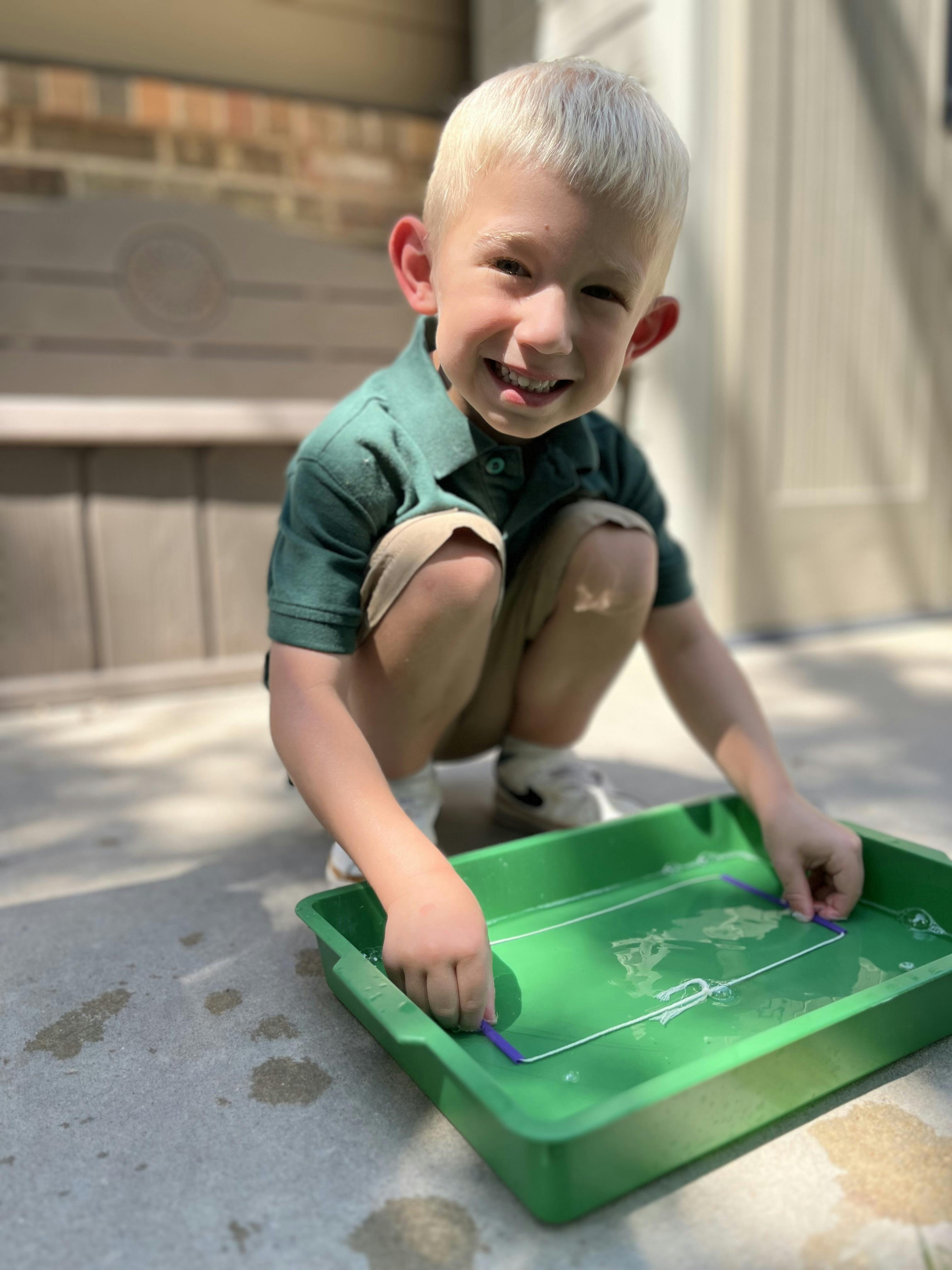 Child crouching and playing with a green tray of water