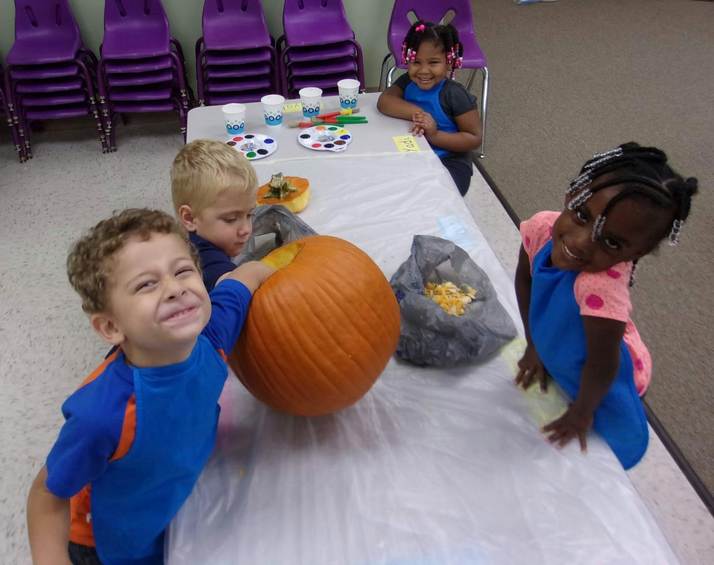 Children at a table with a pumpkin and art supplies