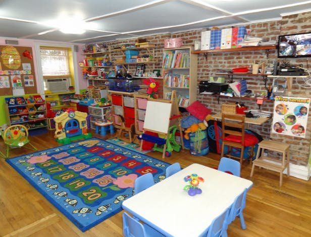 A classroom with a number rug, small tables, and shelves filled with toys and books