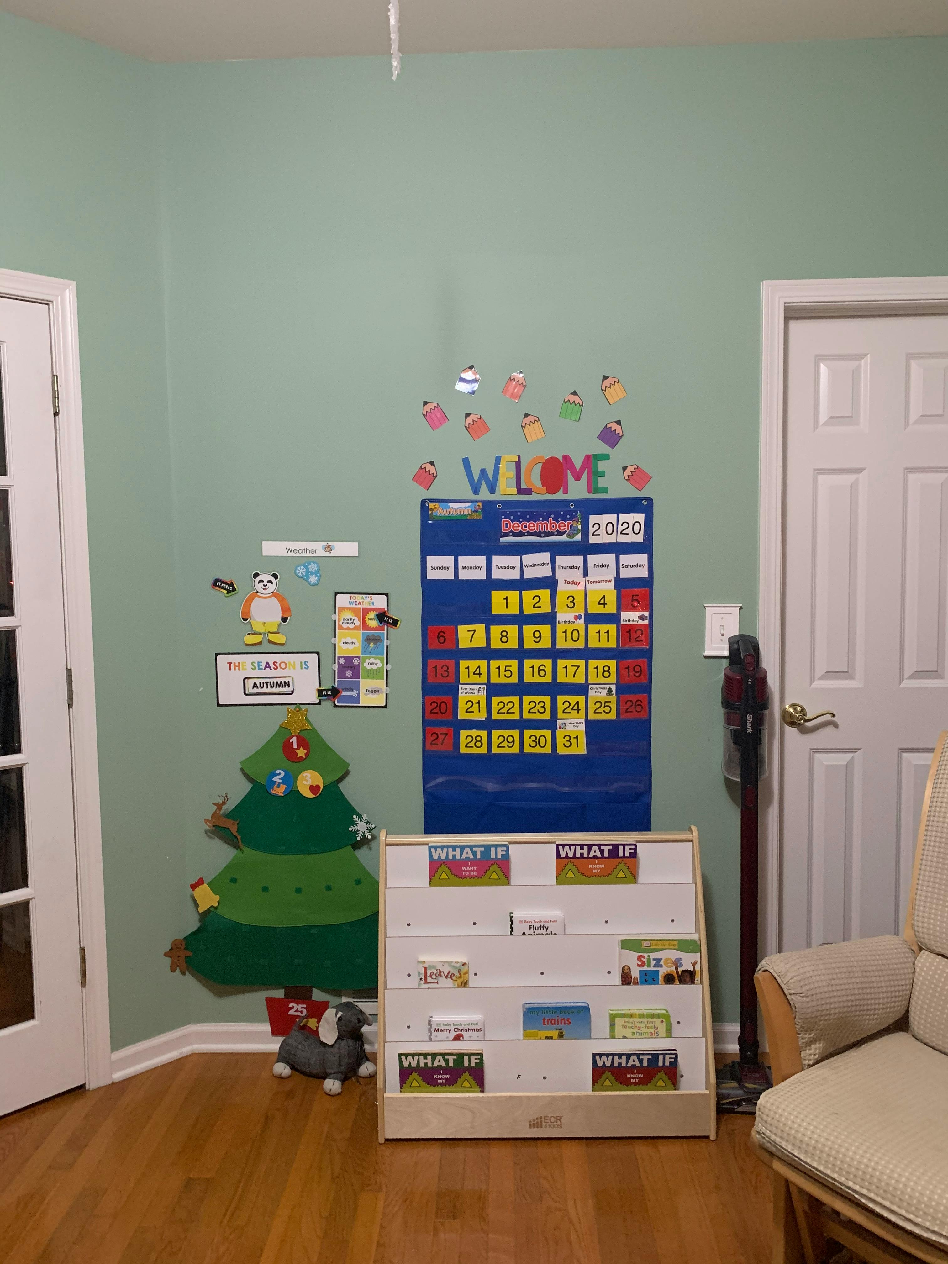 Wall decorated with a calendar, felt Christmas tree, and a book display