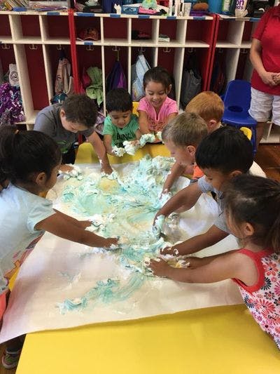 Children playing with shaving cream on a table in a classroom