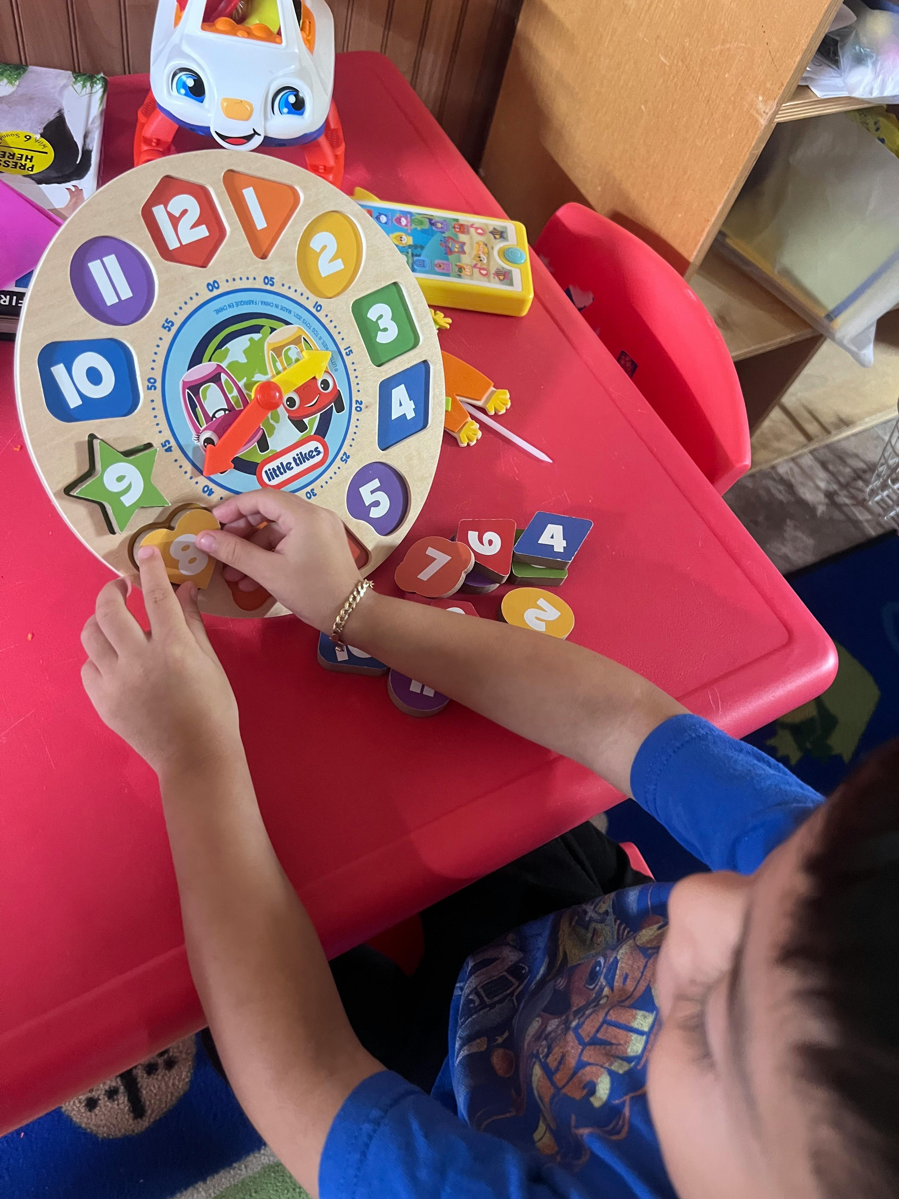 Child playing with a wooden clock puzzle on a red table