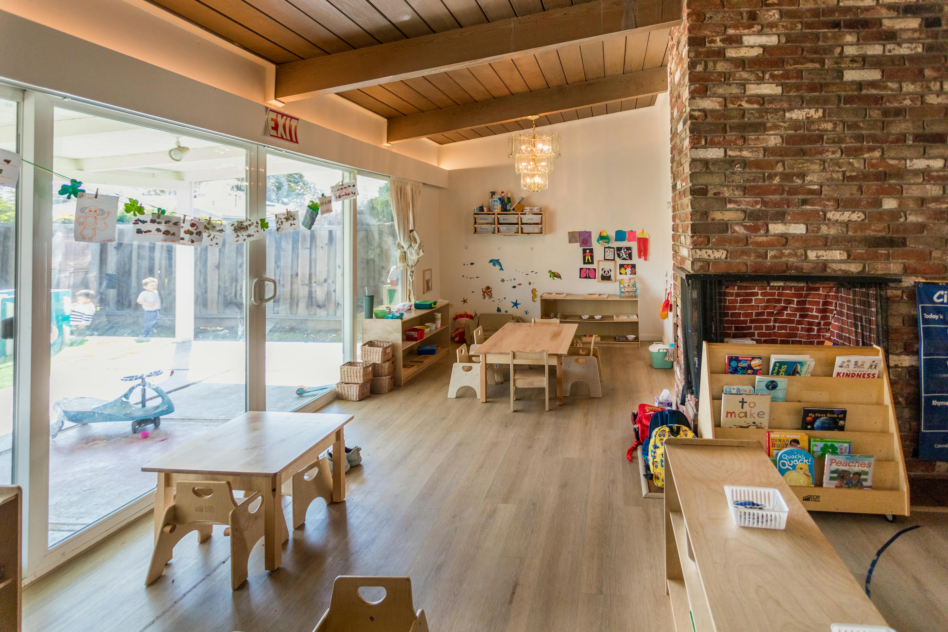Classroom with small tables and chairs, large windows, and a brick fireplace