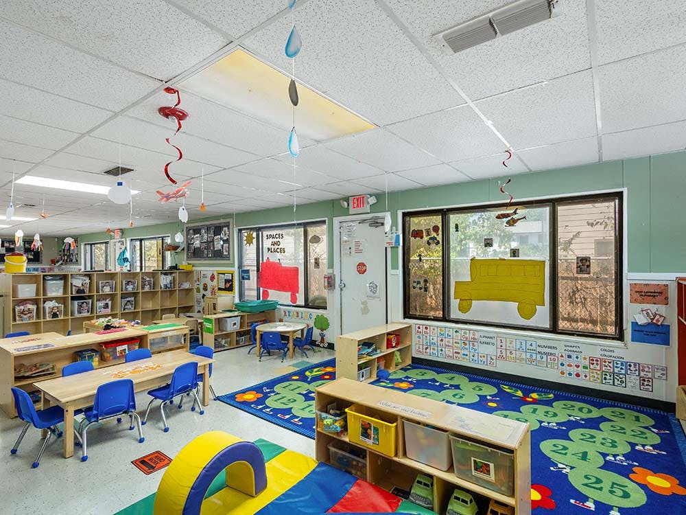 Empty colorful preschool classroom with tables, chairs, and learning rugs