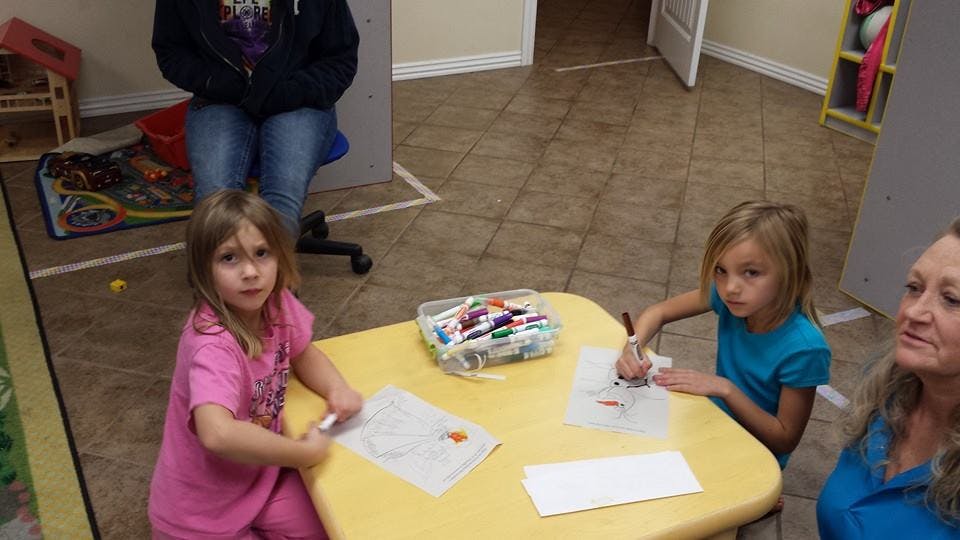 Two children drawing at a table with an adult nearby