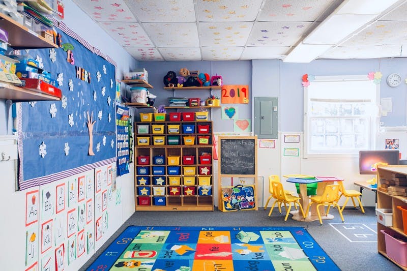 Empty classroom with colorful storage, small tables, and a patterned rug