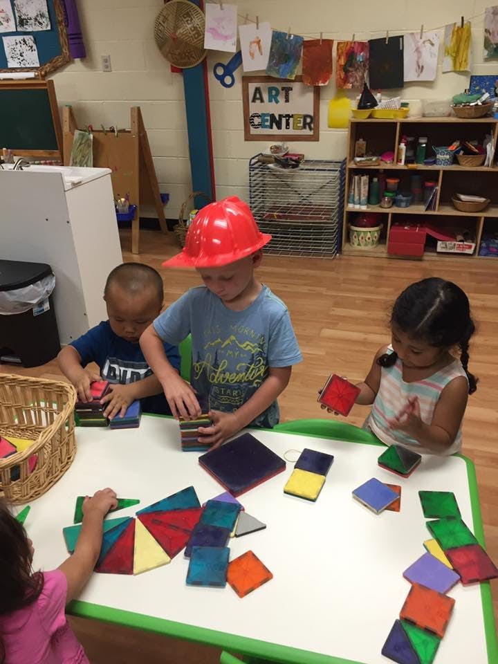 Children playing with colorful magnetic tiles at a table in a classroom