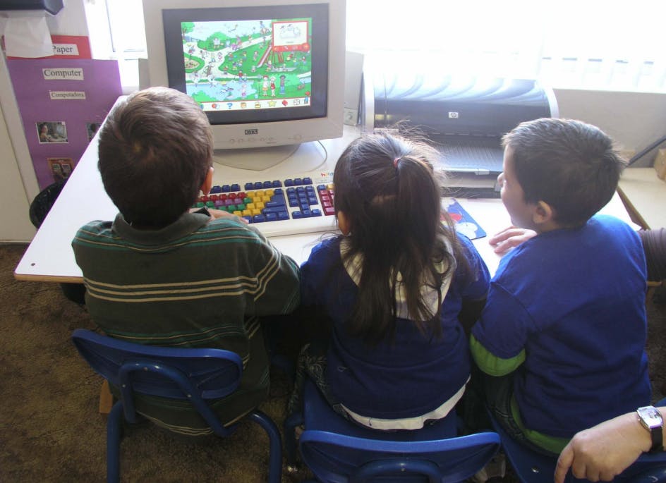Three children sitting at a desk looking at a computer screen
