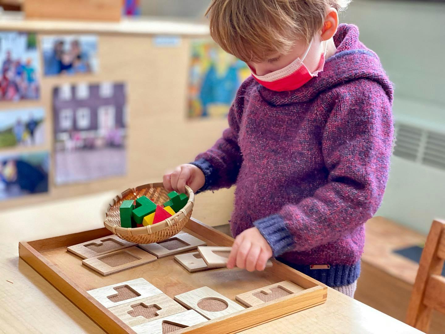 Child in a mask playing with wooden shape puzzles and block puzzles in a classroom