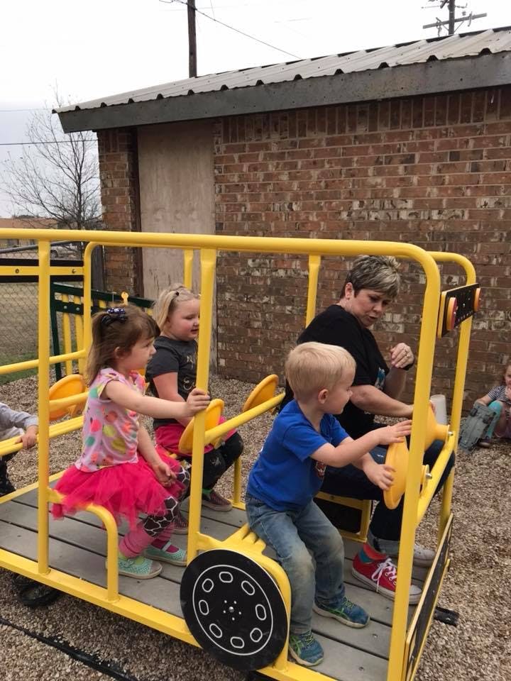Adult and children playing on a yellow bus-shaped playground structure