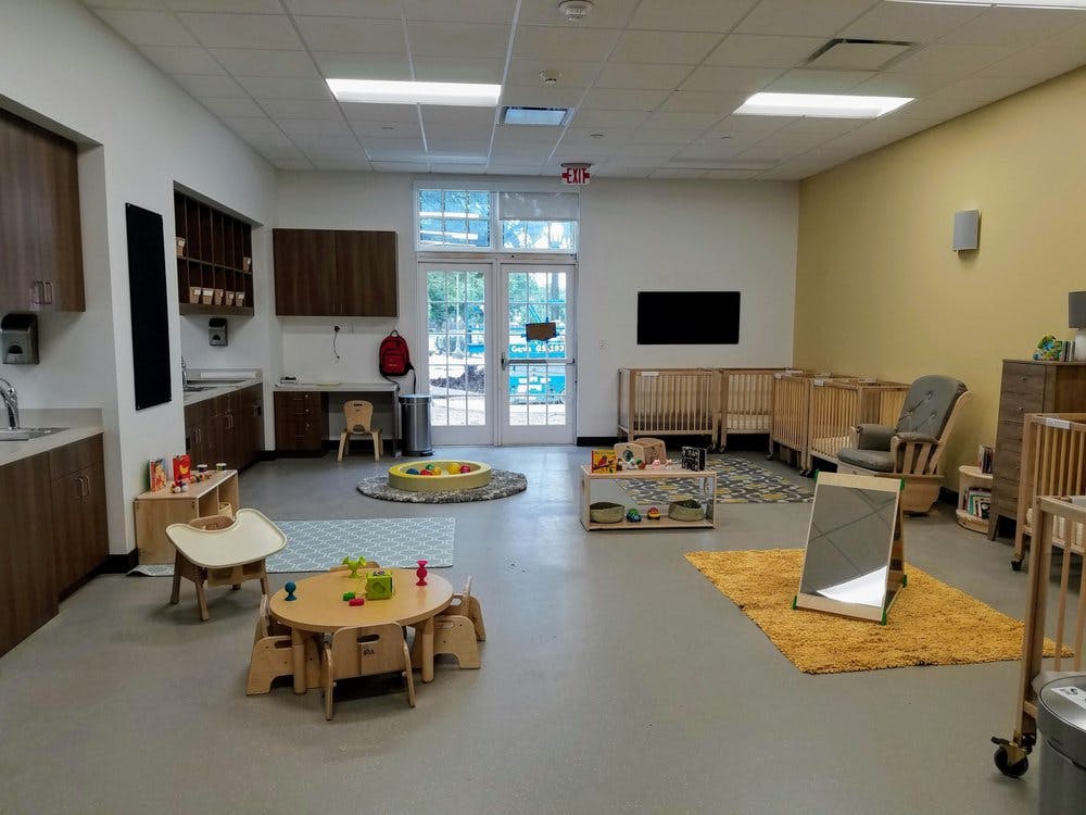 Empty classroom with small tables, chairs, cribs, and a play area