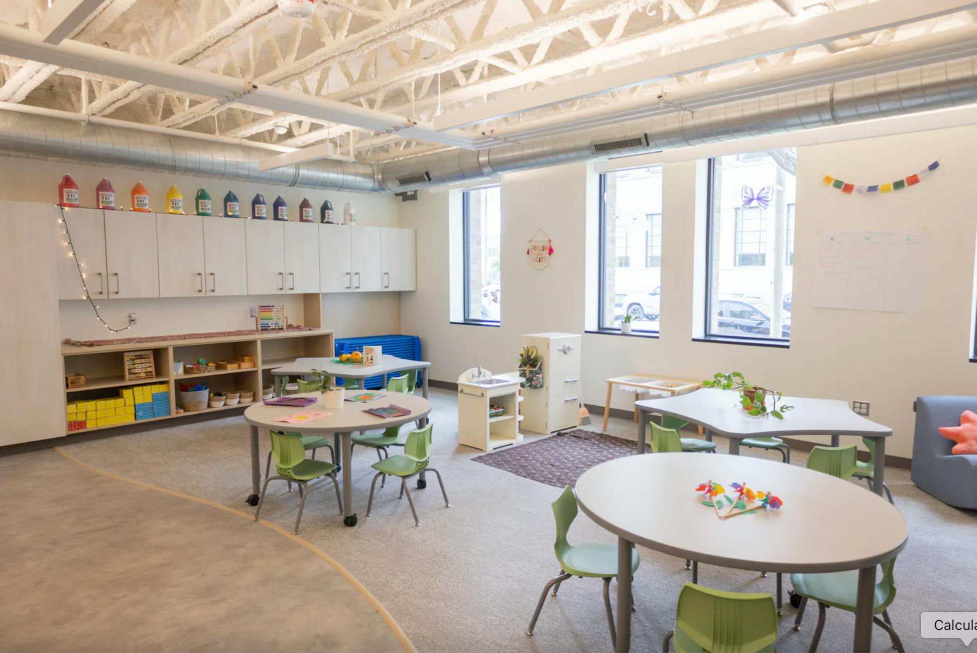 Classroom with multiple small tables, chairs, and learning materials on shelves