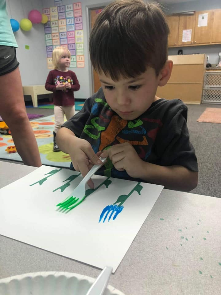 Child using a fork to paint on paper