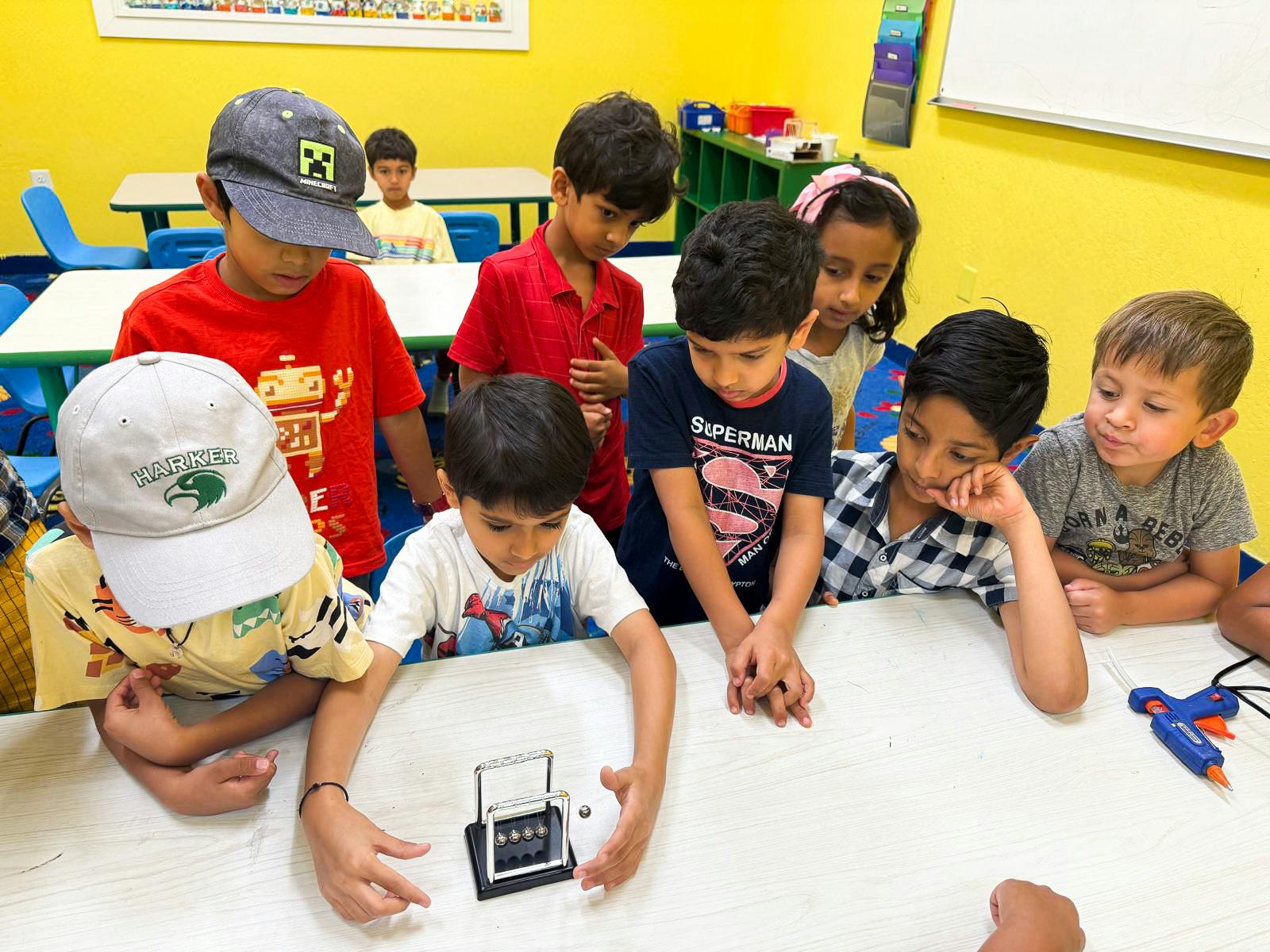 Children gathered around a table looking at a Newton's Cradle