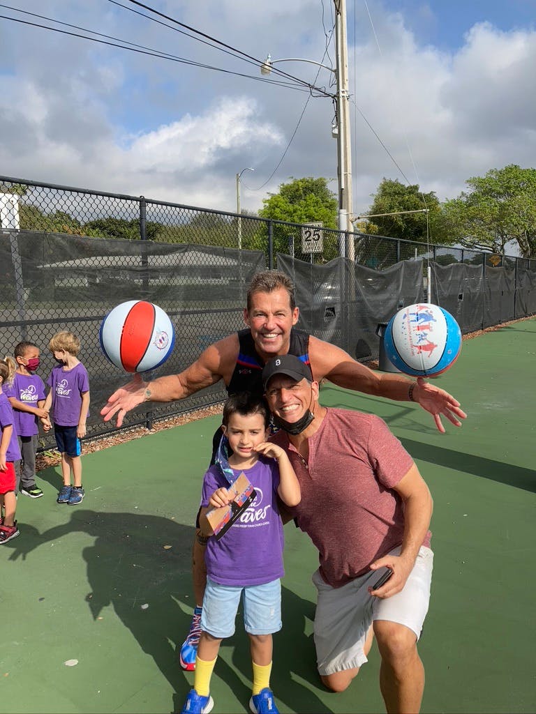 Two adults and a child posing with two beach balls on a court