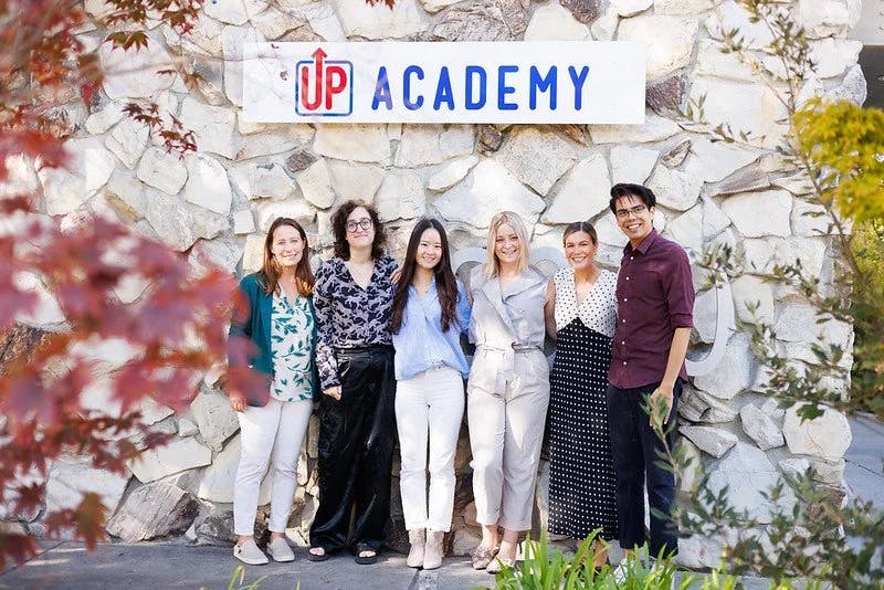 Six people standing in front of a stone wall with a sign that reads "UP ACADEMY"