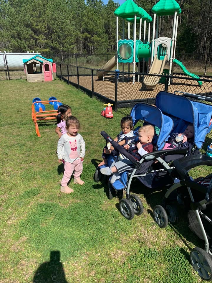 Children and babies in strollers on grass near a playground