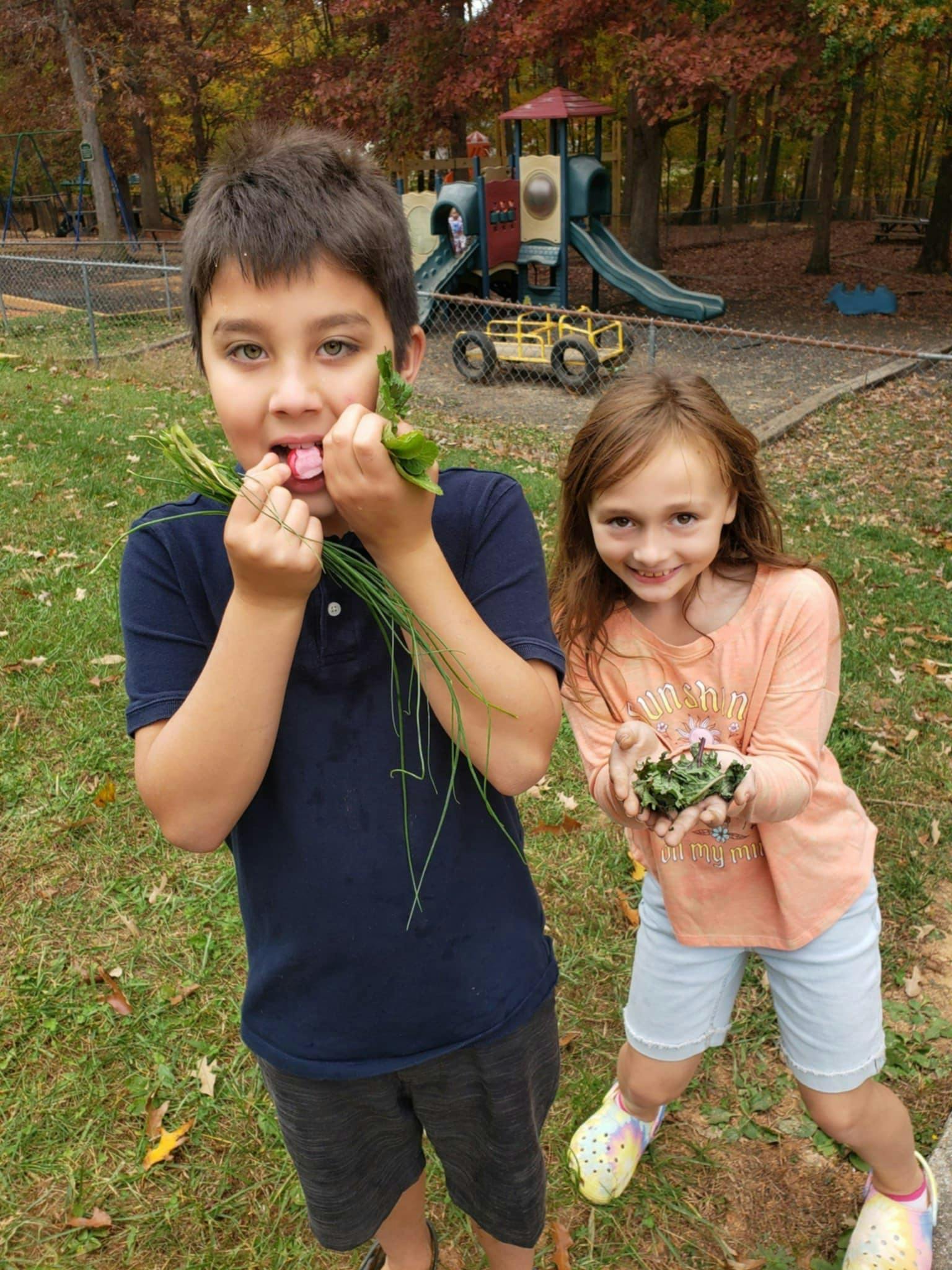 Child holding green plants in mouth, another child holding plants in hands