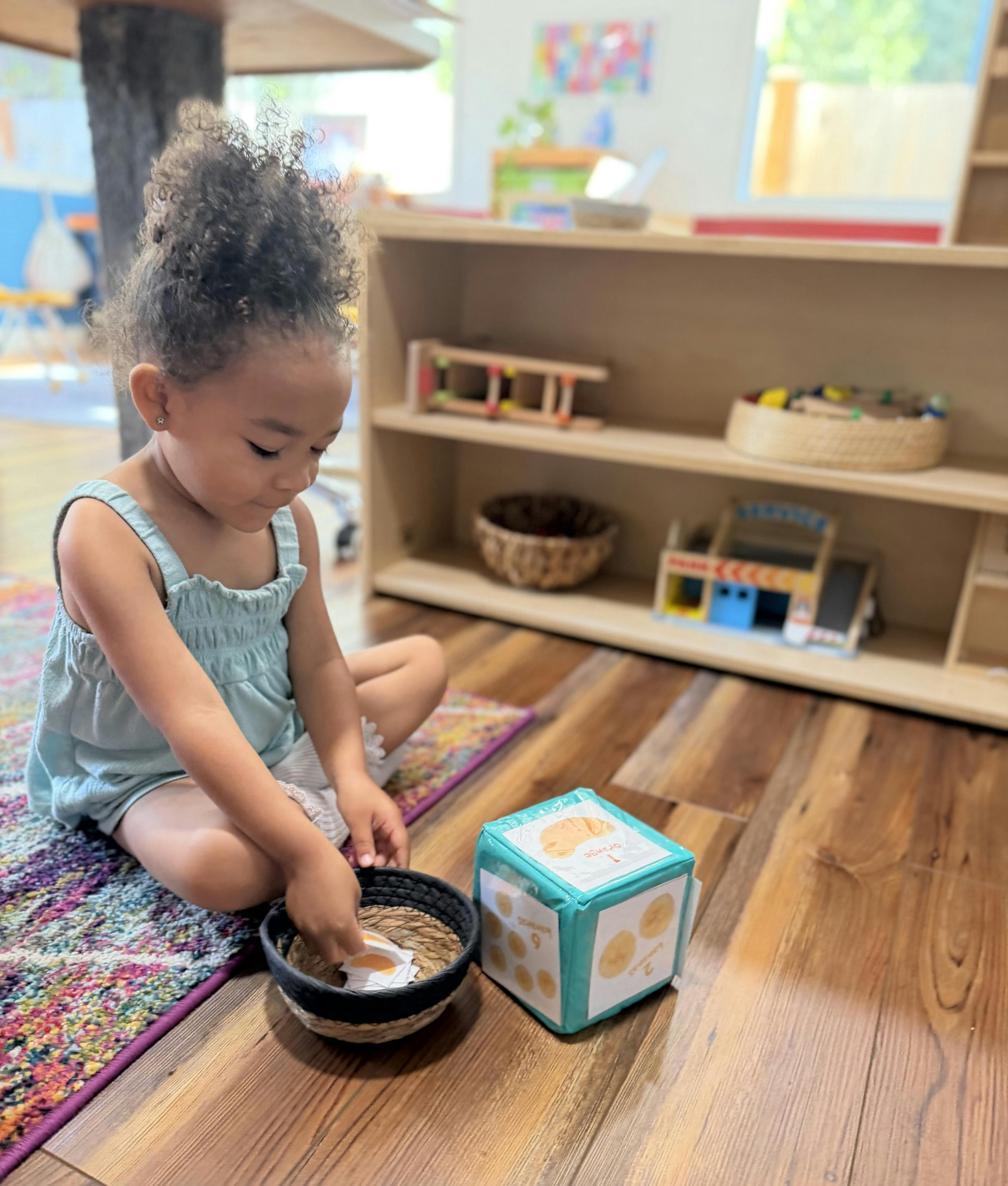 Child sitting on a rug and playing with a foam number cube in a classroom