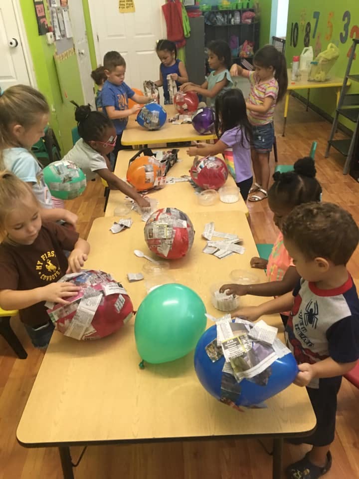Children making paper mache over balloons at tables