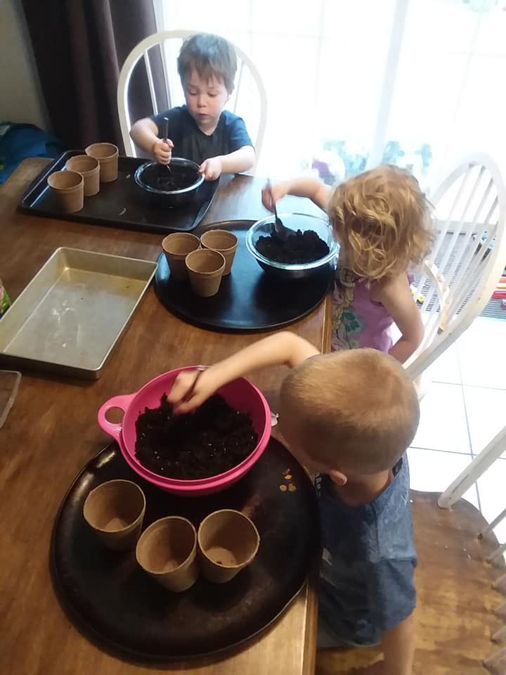 Three children planting seeds in small pots at a table
