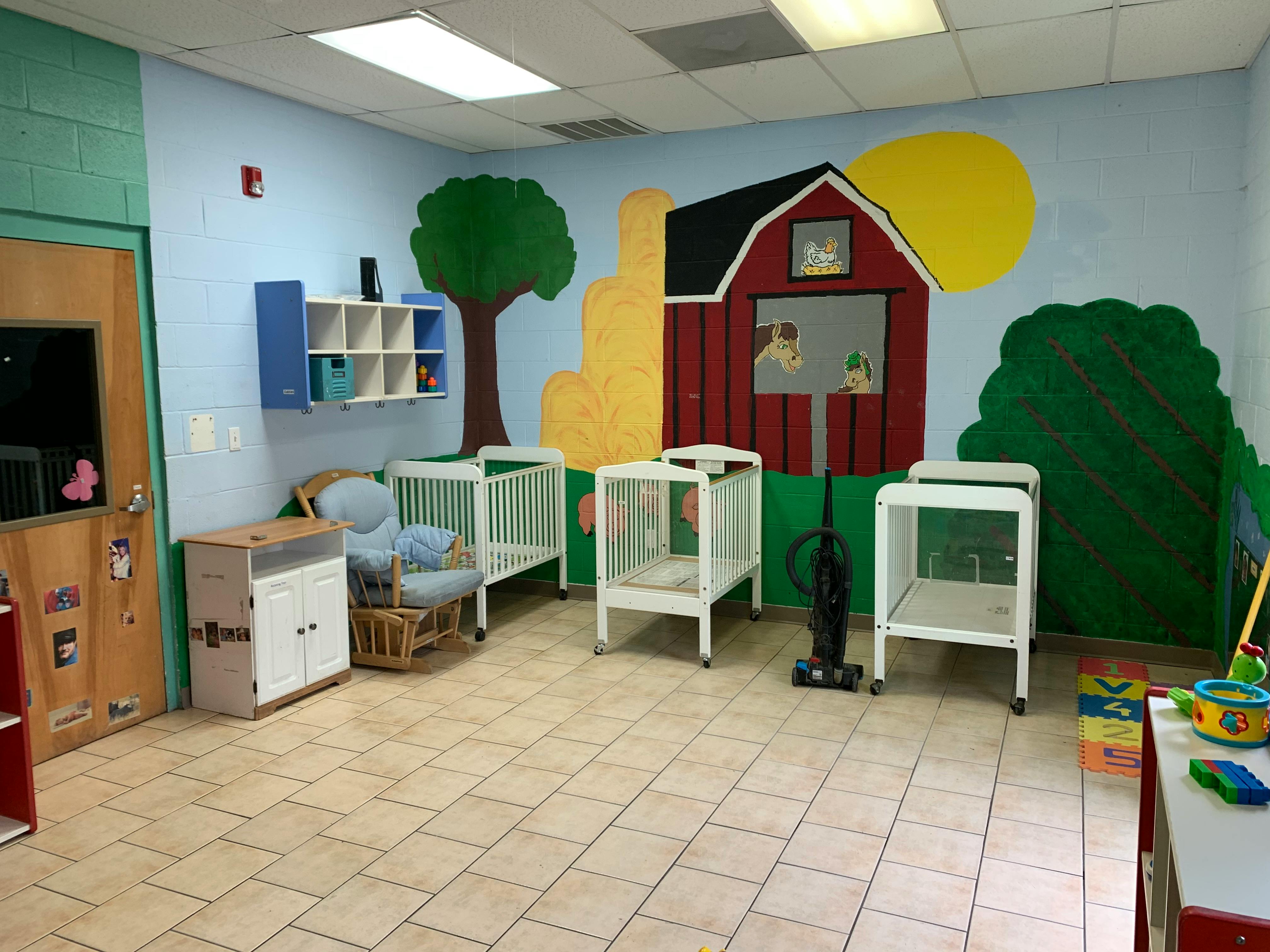 A room with a mural of a farm scene and three baby cribs
