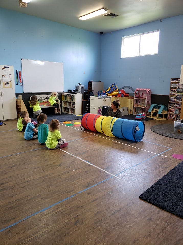 Children sitting on the floor in a classroom with a person and a play tunnel
