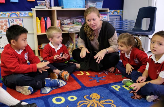 Adult and multiple children sitting on a colorful rug in a classroom
