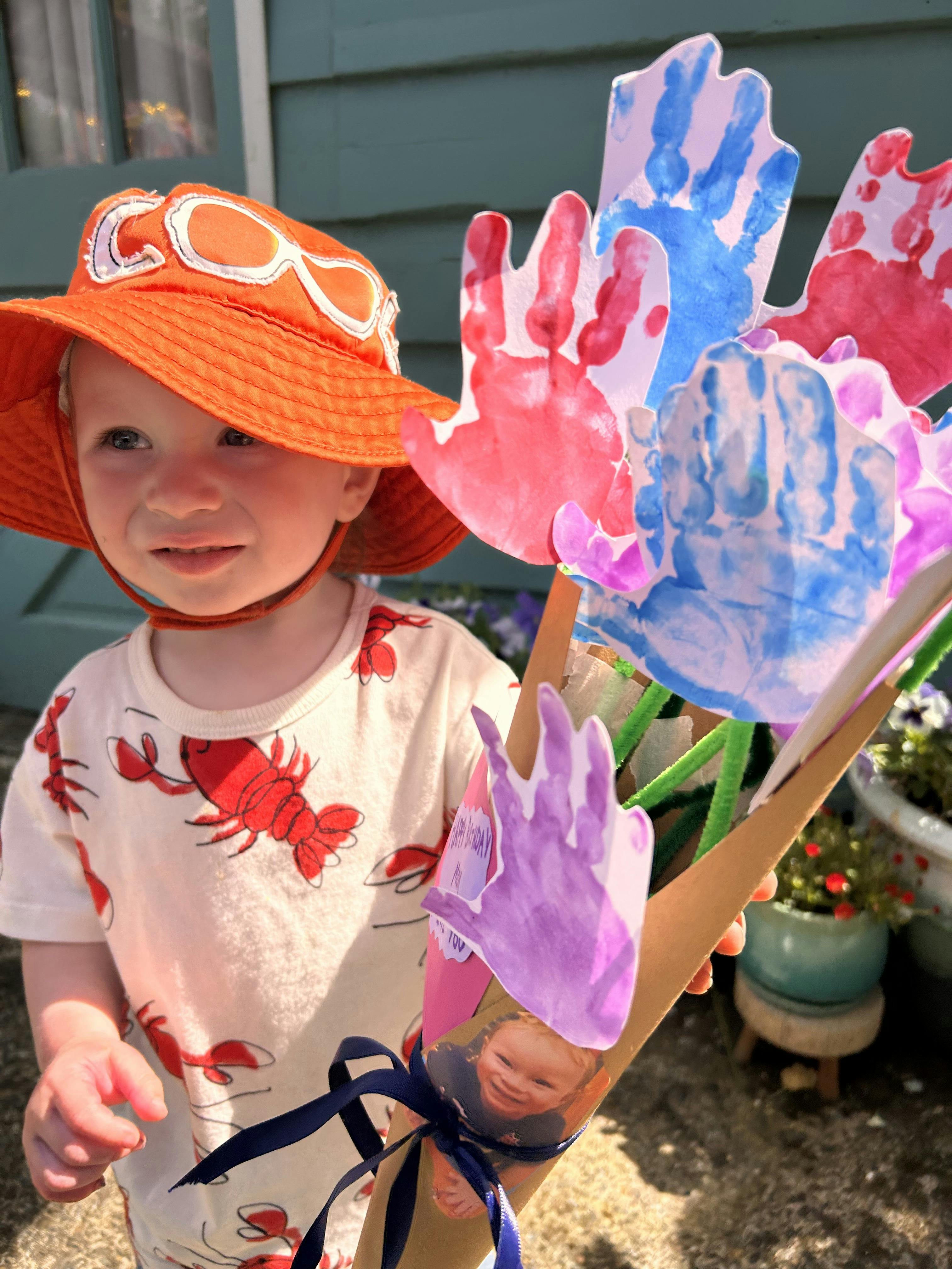 Child wearing an orange hat holding a bouquet of handprint cutouts