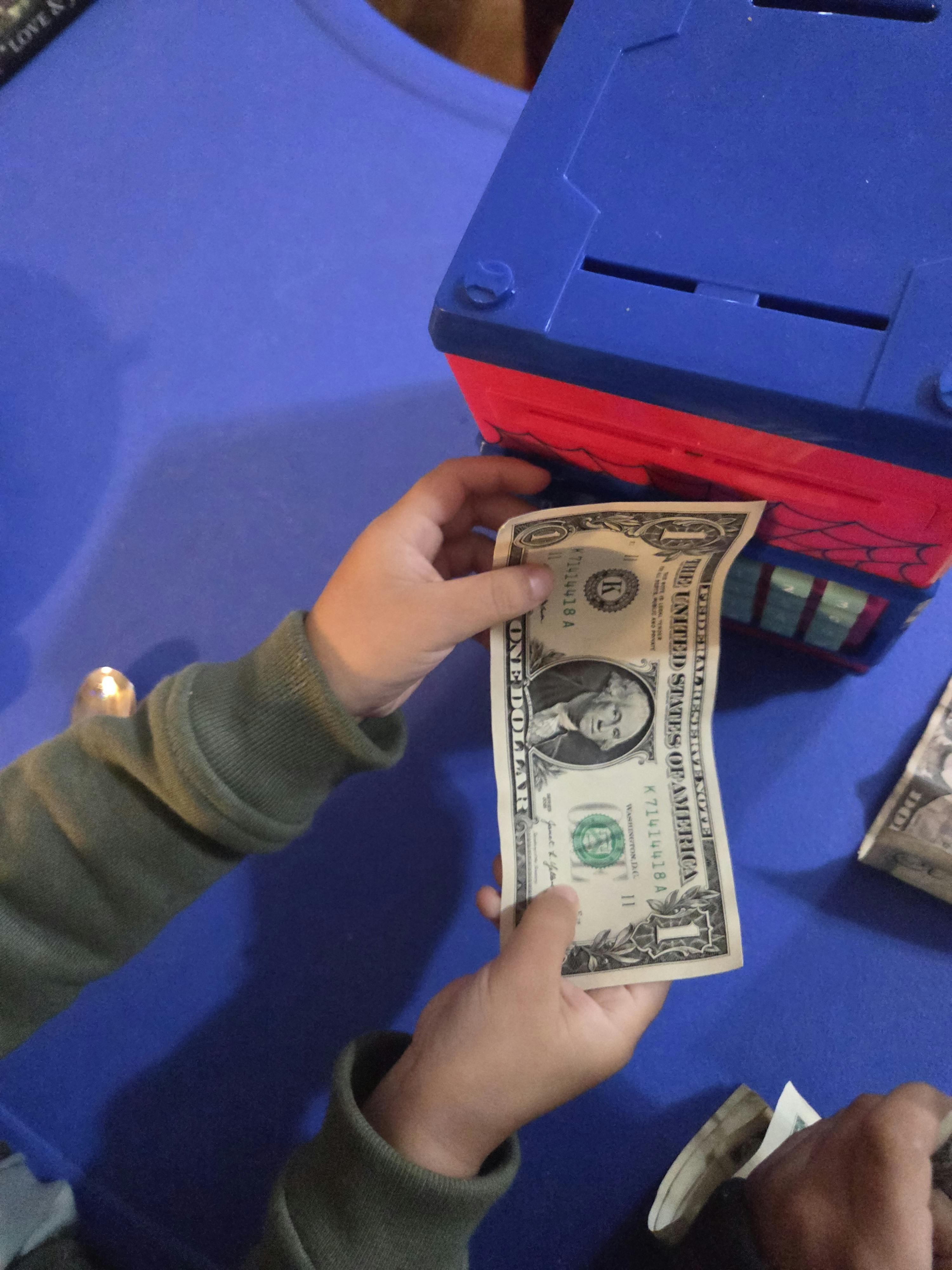 Child's hands holding a dollar bill near a blue and red toy