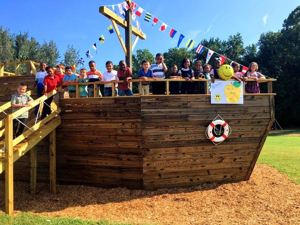 Children standing on a wooden play structure shaped like a ship
