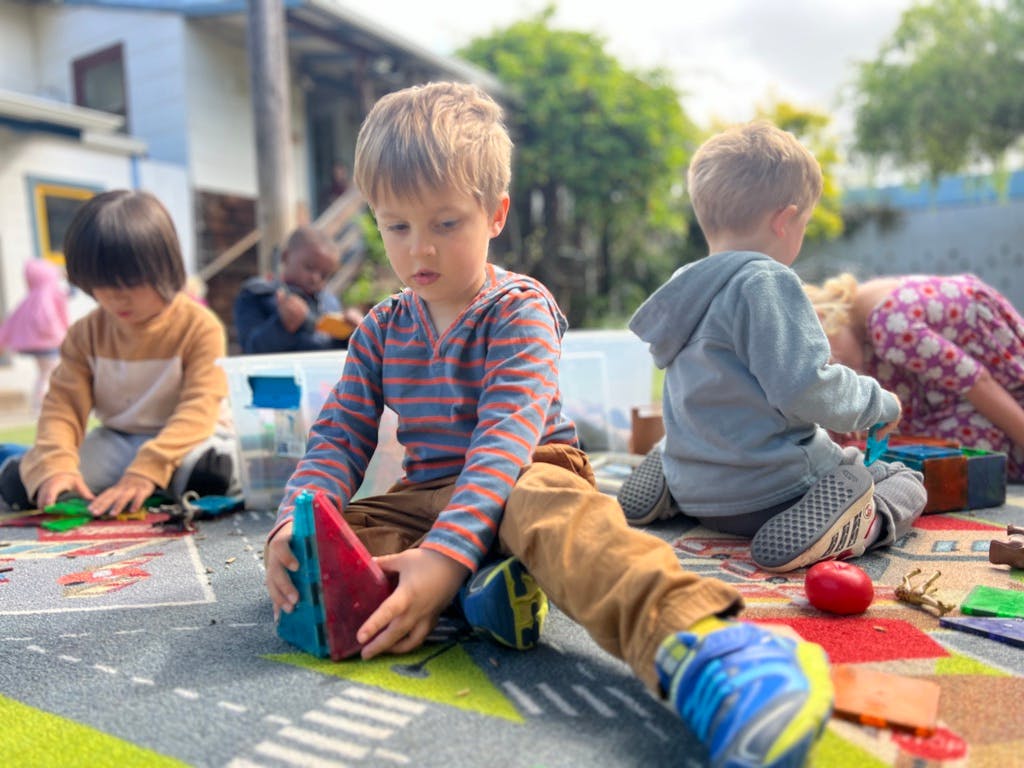Children playing with toys on a mat outdoors