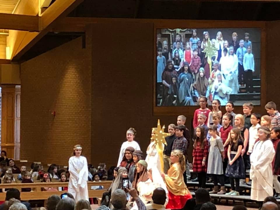 Children performing on a stage with a large screen displaying more children