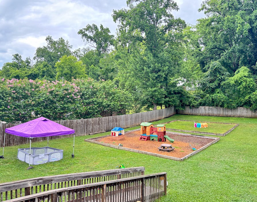 Playground equipment and a purple canopy tent in a fenced backyard