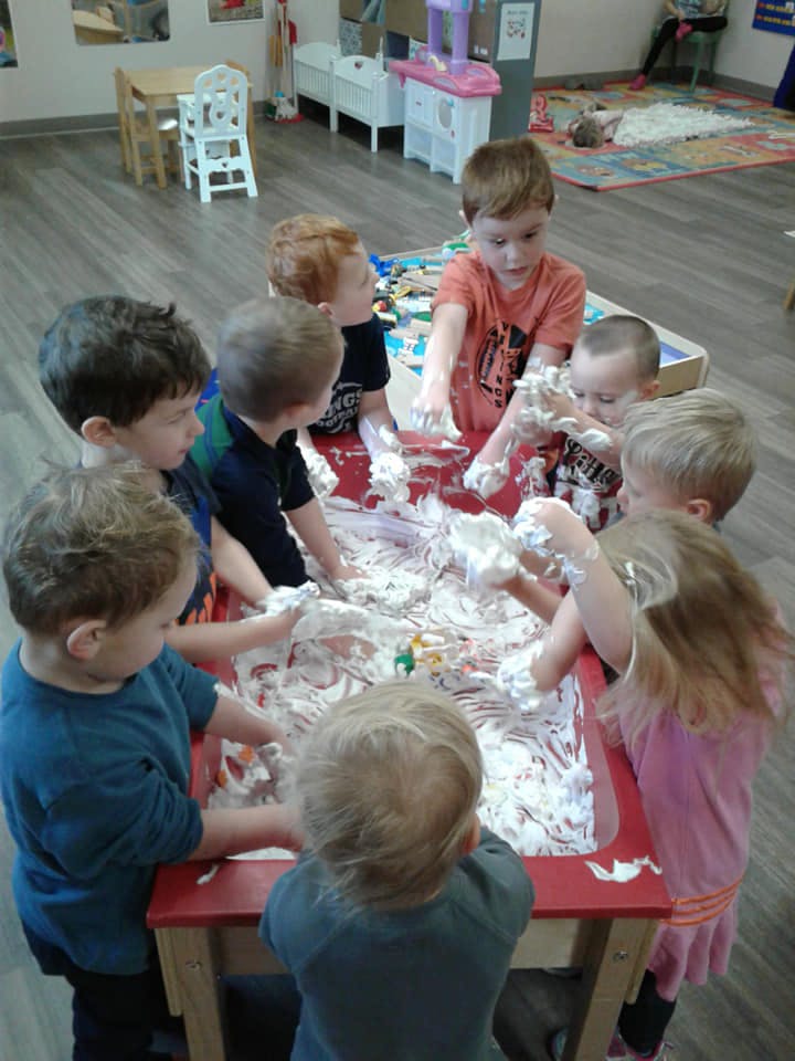 Children playing with shaving cream at a red table