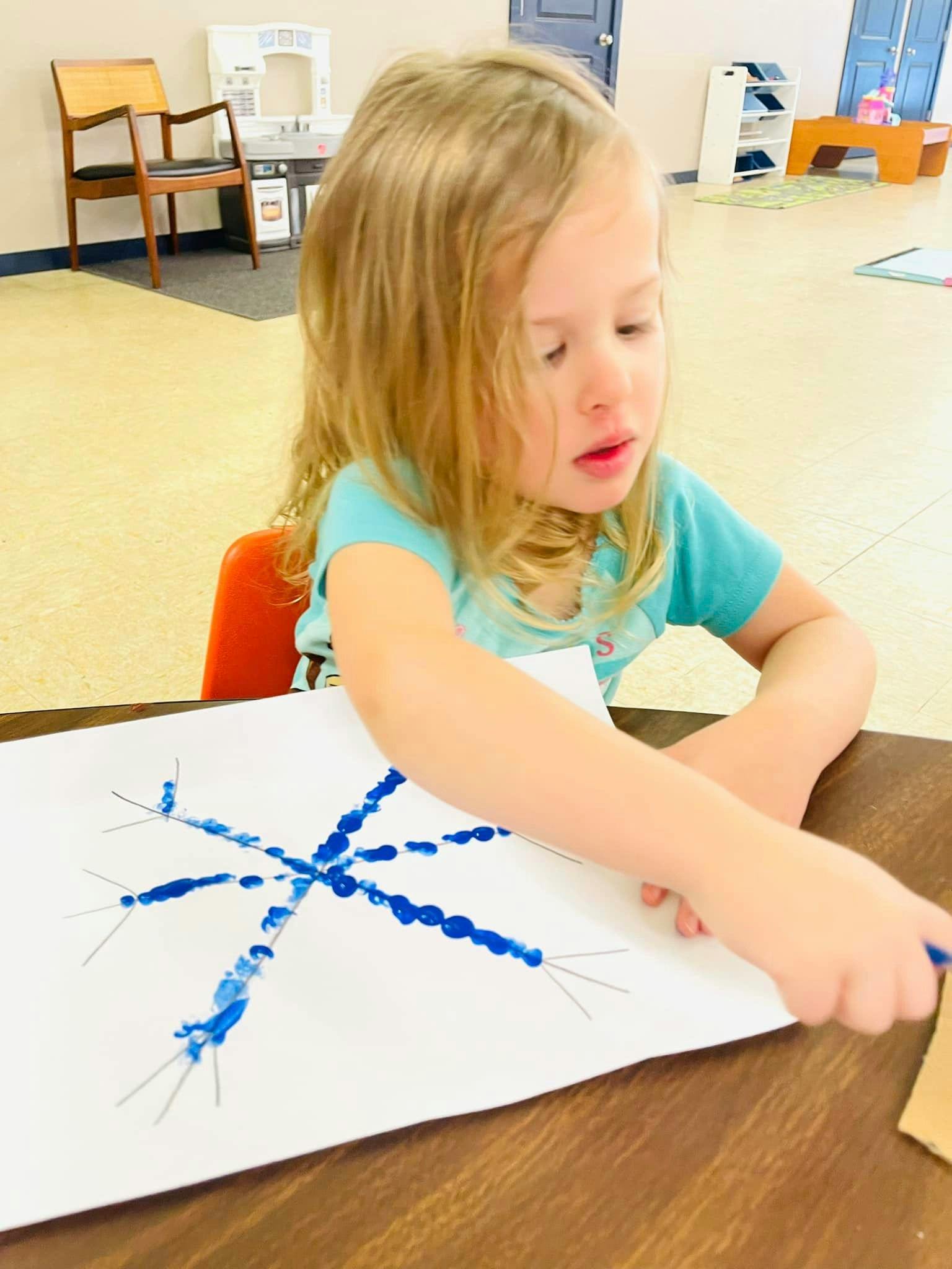 Child painting a blue snowflake design on paper