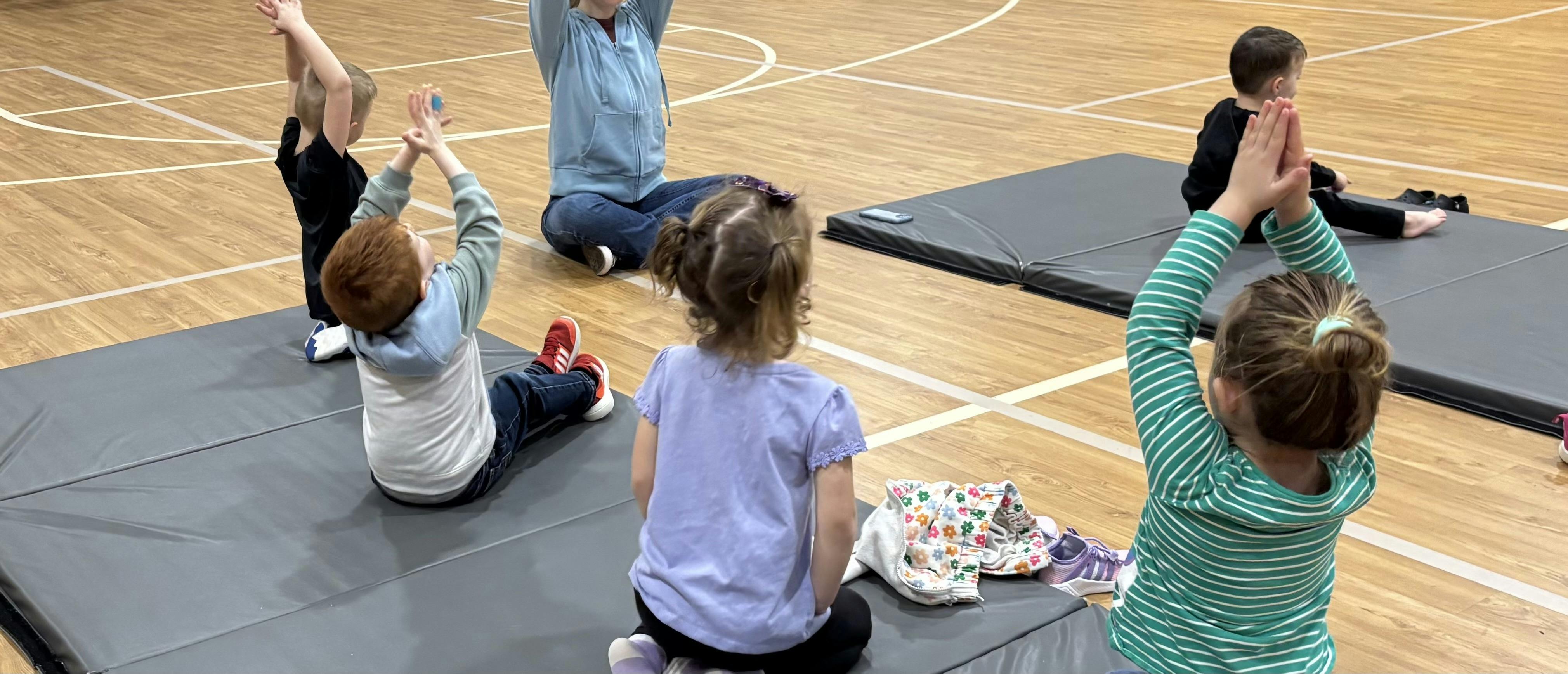 Children and a person doing exercises on mats in a gymnasium