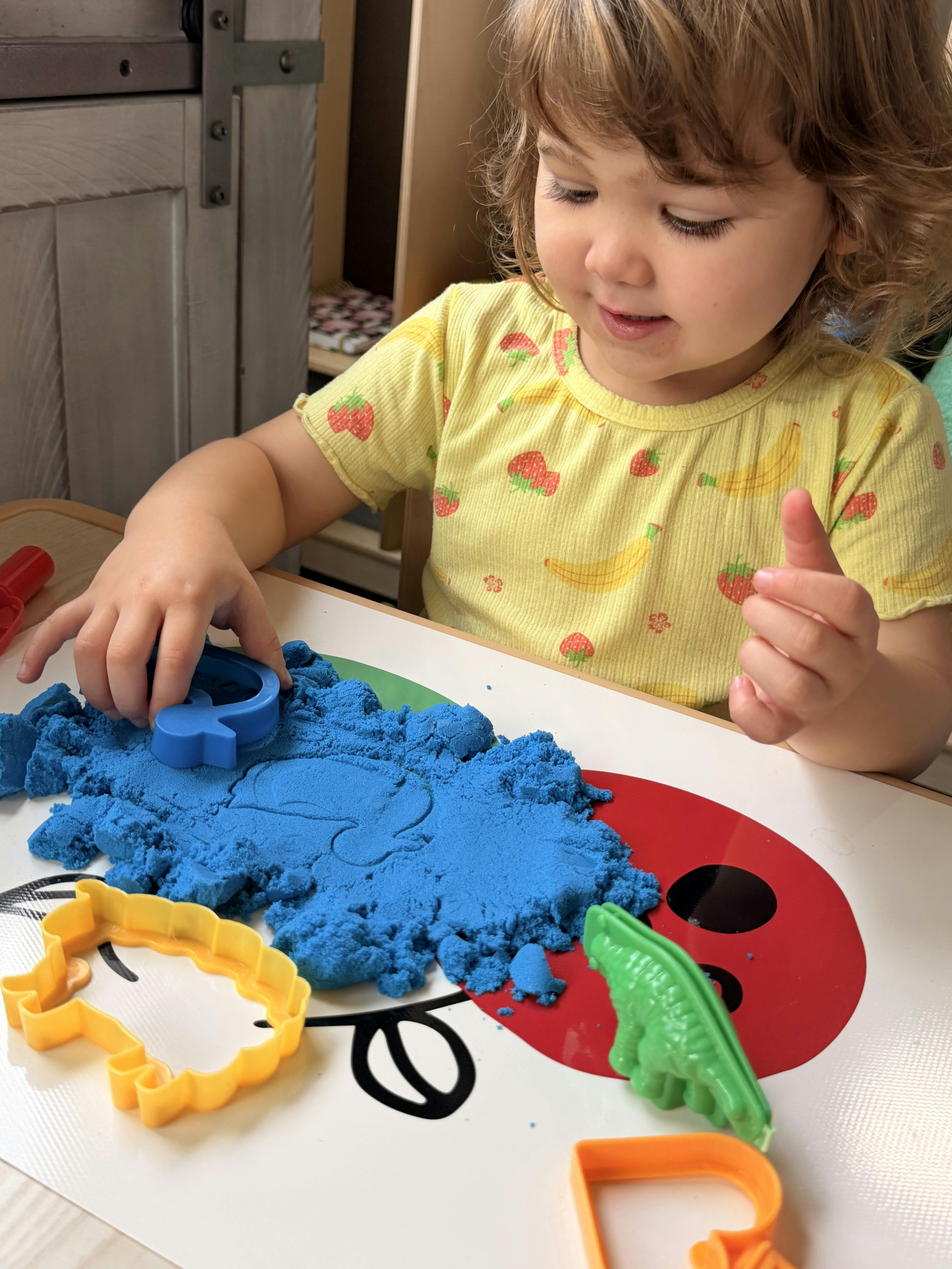 Child playing with blue kinetic sand and cookie cutters on a table