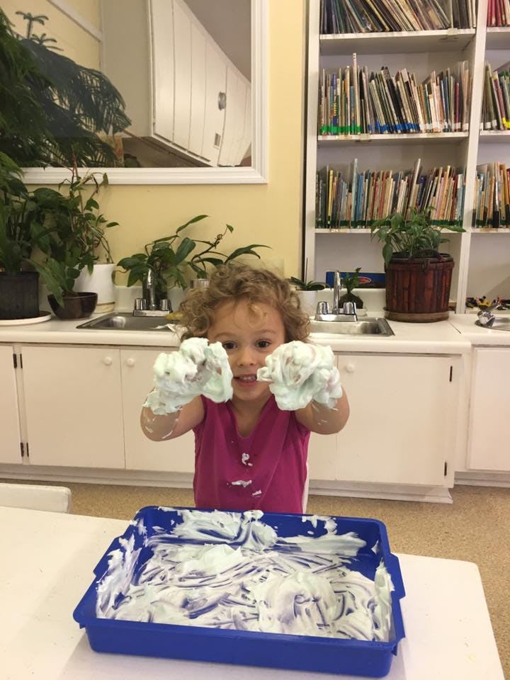 Child with shaving cream on hands and in a blue tray