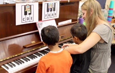 Adult teaching two children to play piano