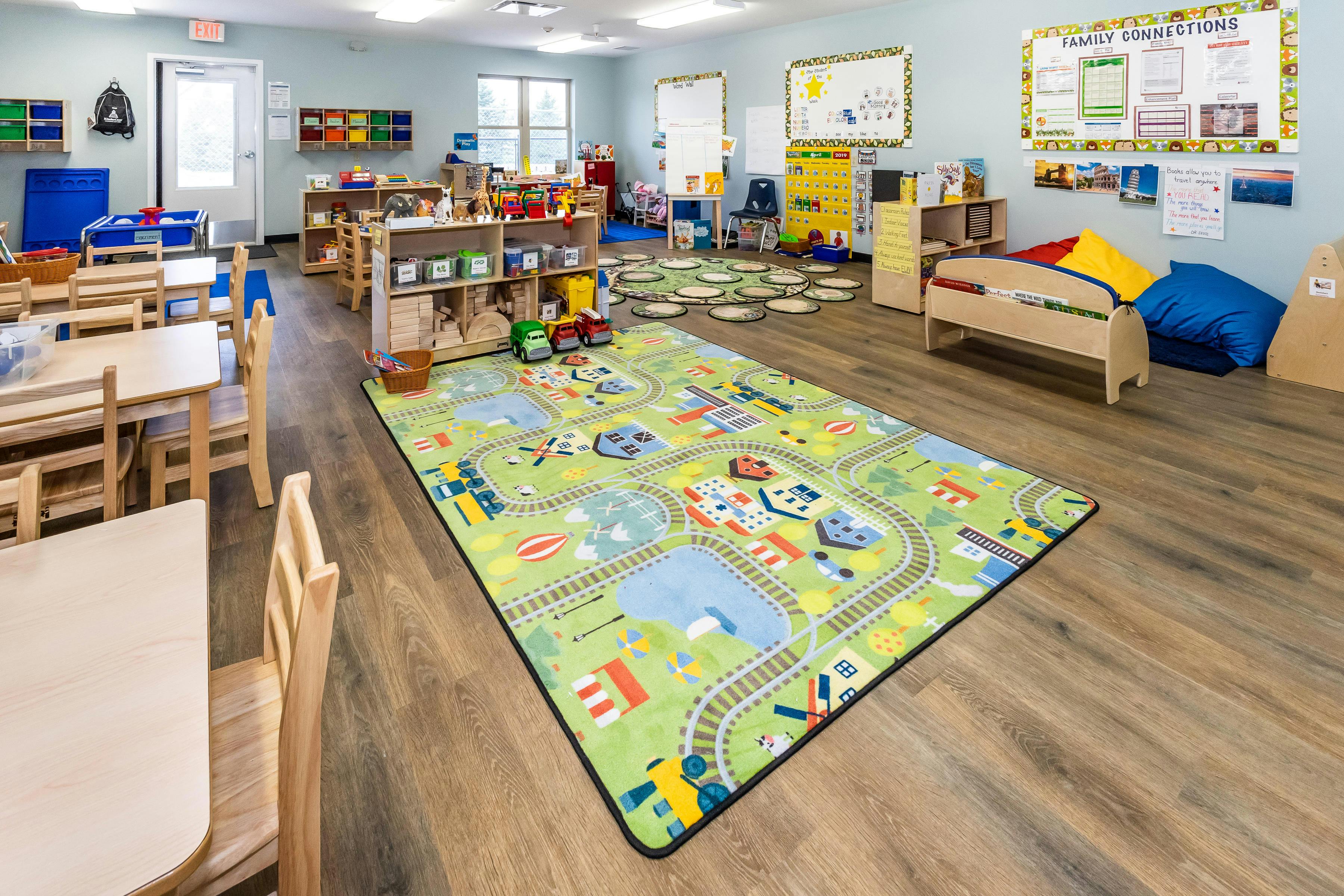 Colorful rug on the floor of an empty classroom with small tables, chairs, and shelves