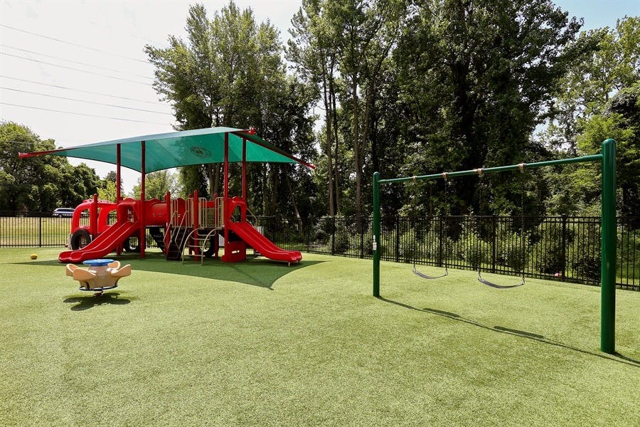 Playground with red slides, green canopy, and swings on artificial turf