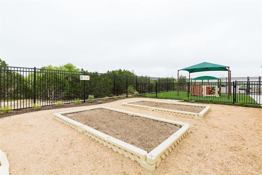 Two empty raised garden beds with a fenced area and green canopy in the background