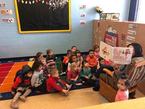 Person reading a book to a group of children in a classroom