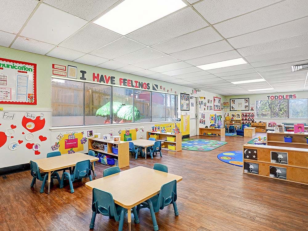 Classroom with small tables and chairs, shelves with toys, and posters on the walls