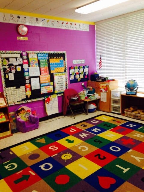 Classroom with a colorful alphabet rug, bulletin board, and small chairs