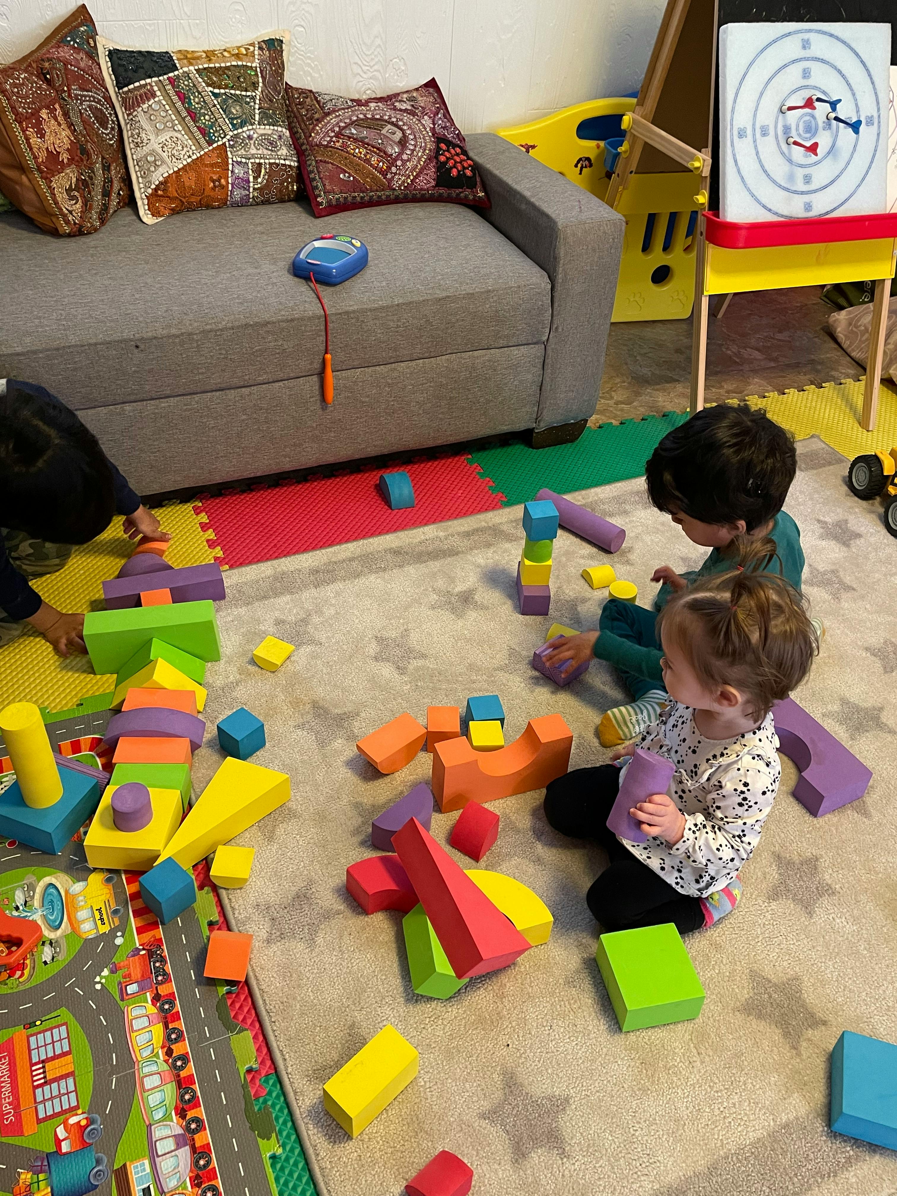 Three children playing with colorful building blocks on a rug