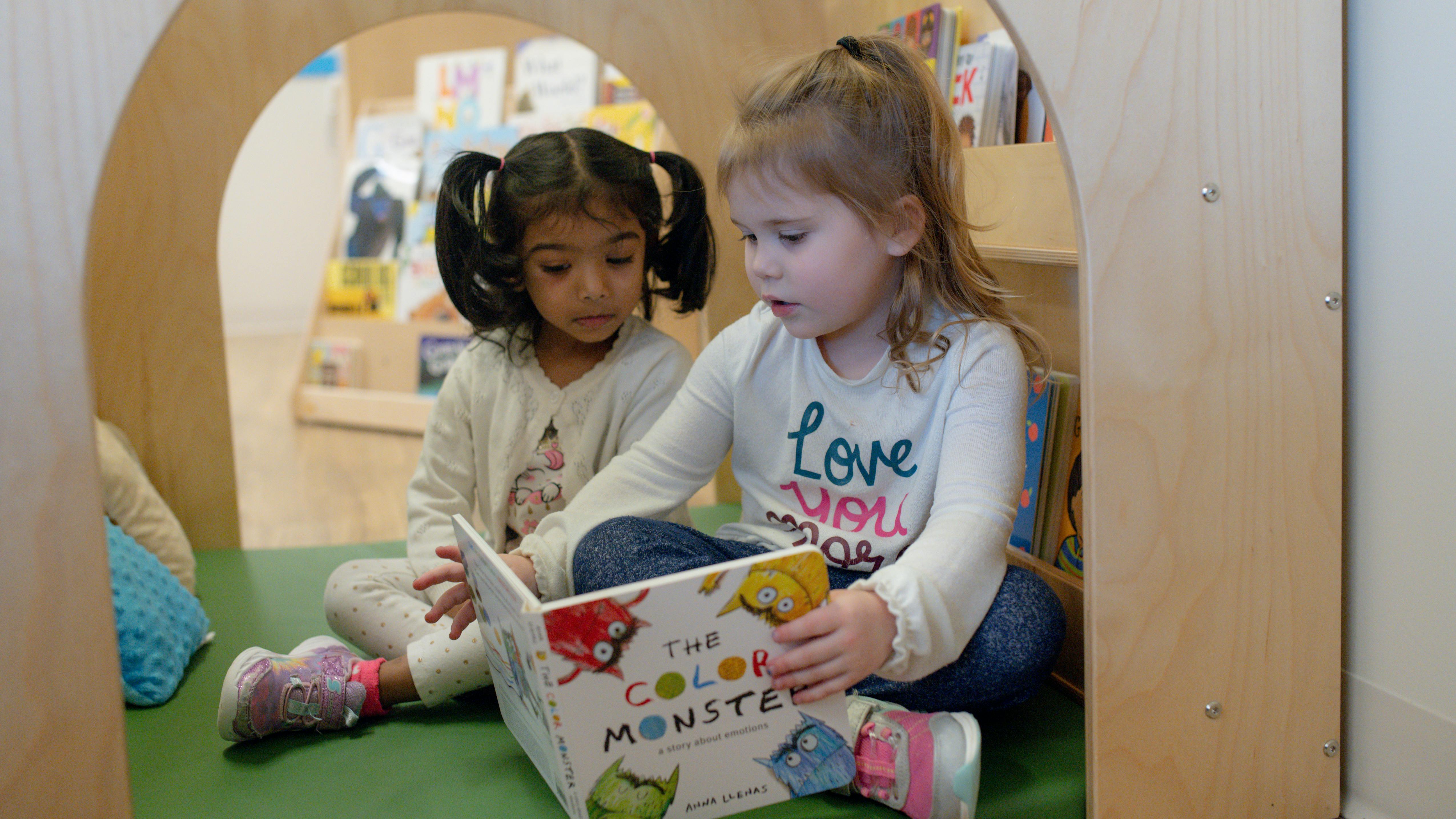Two children sitting on the floor reading a book together